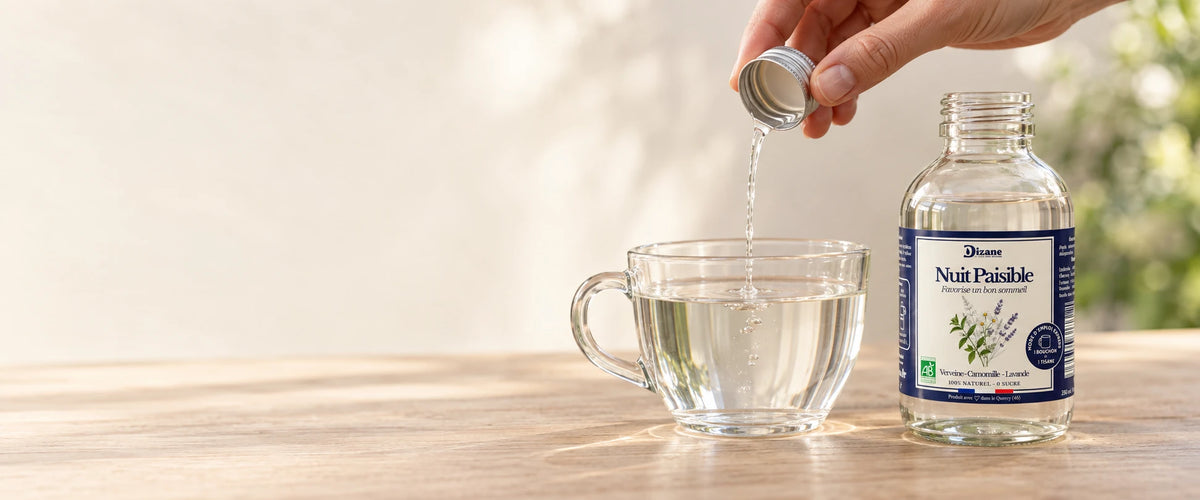 Un bouchon de Dizane Nuit Paisible, tisane bio à diluer, versé dans une tasse d’eau, à côté du flacon.